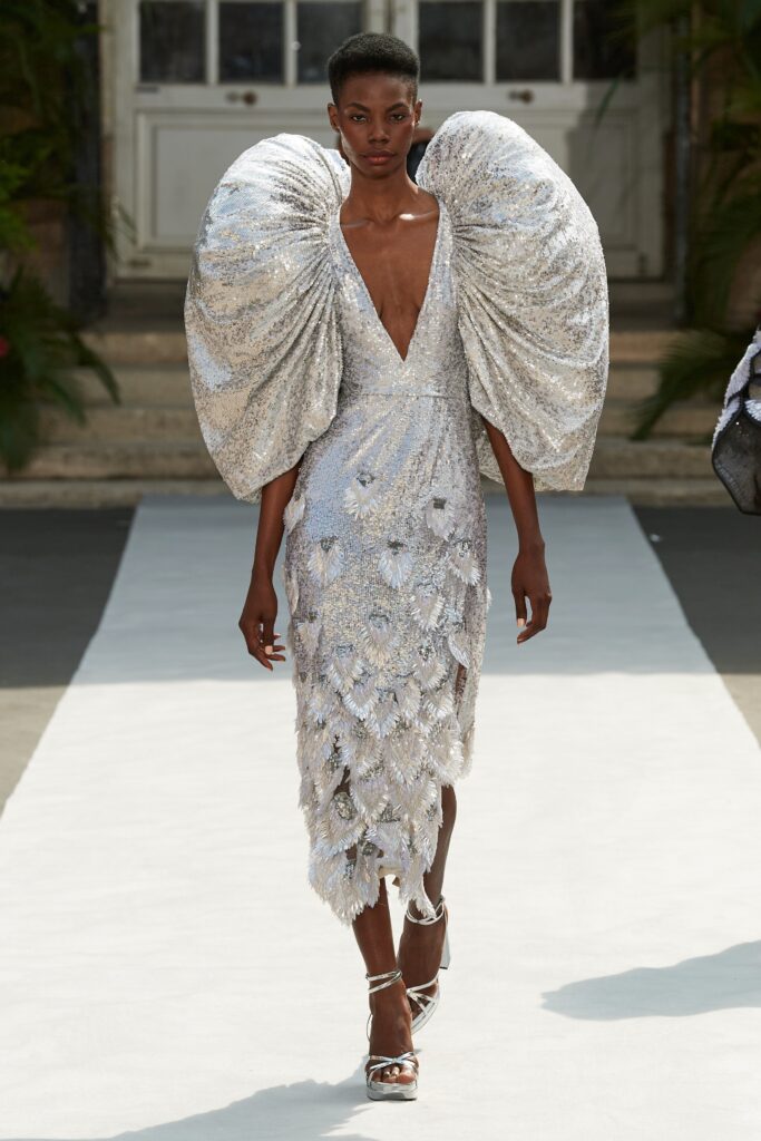 A fitted silver sequin sleeveless dress with a V-neckline and tiered design details.