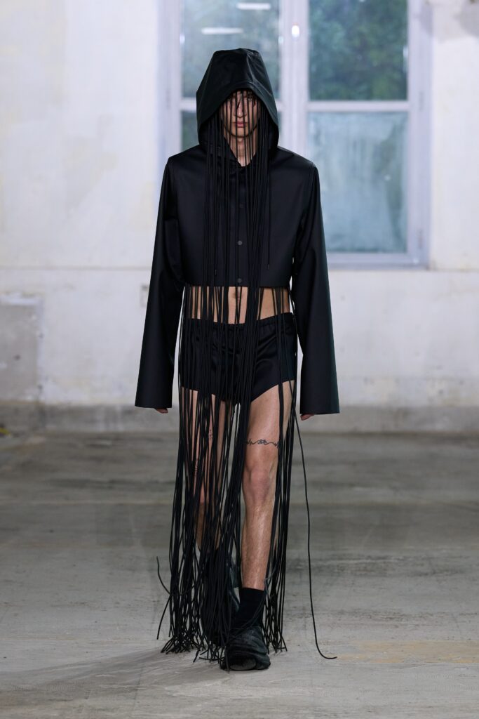 A relaxed black cotton hooded jacket with long sleeves and fringed detailing, paired with shorts.