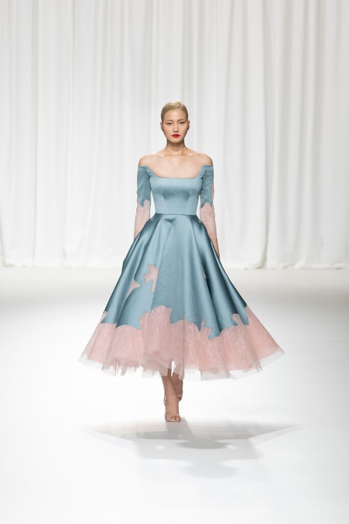 A fitted blue silk off-shoulder dress with long sleeves and a tiered design.