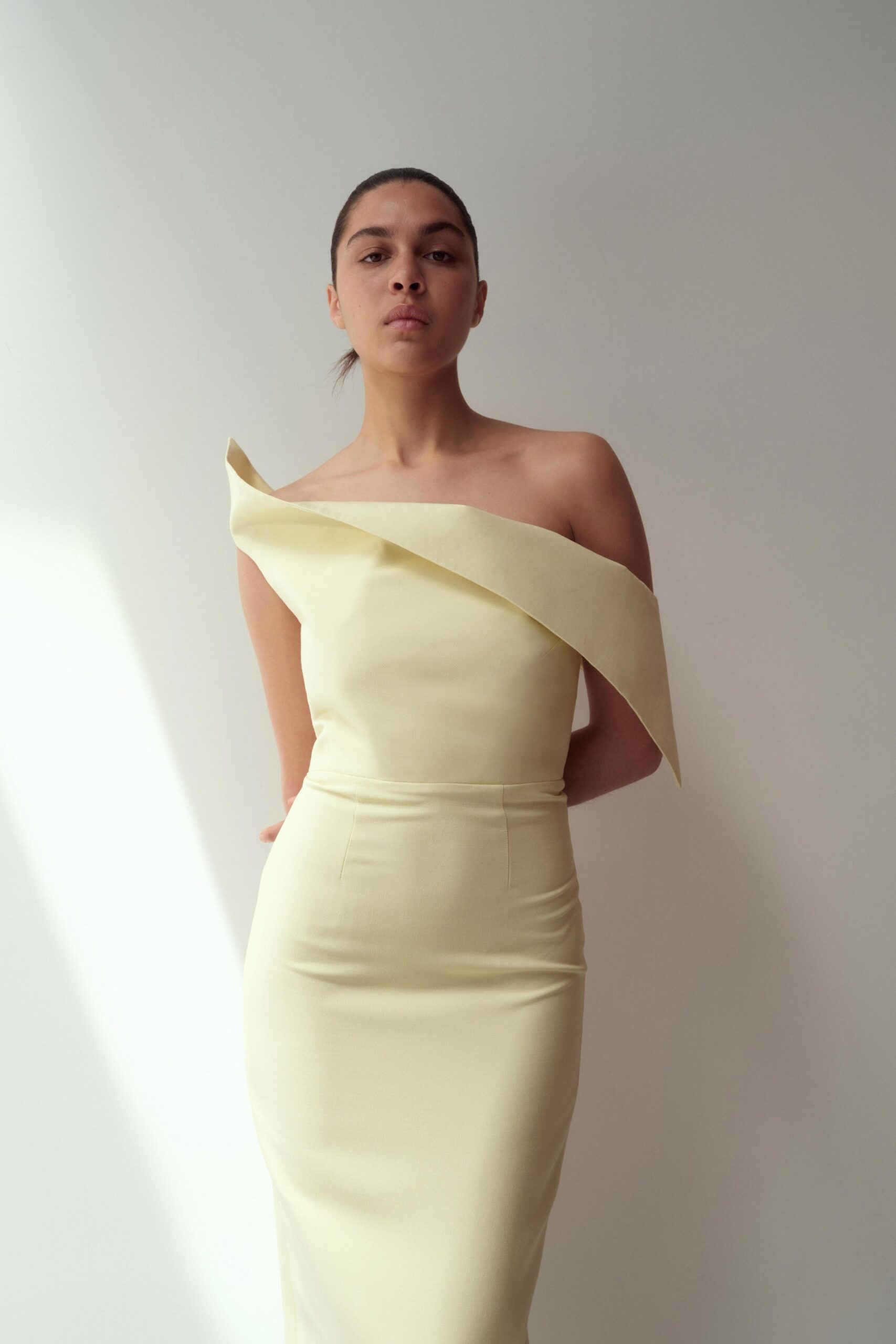 A fitted yellow silk dress with an asymmetric design and sleeveless construction.
