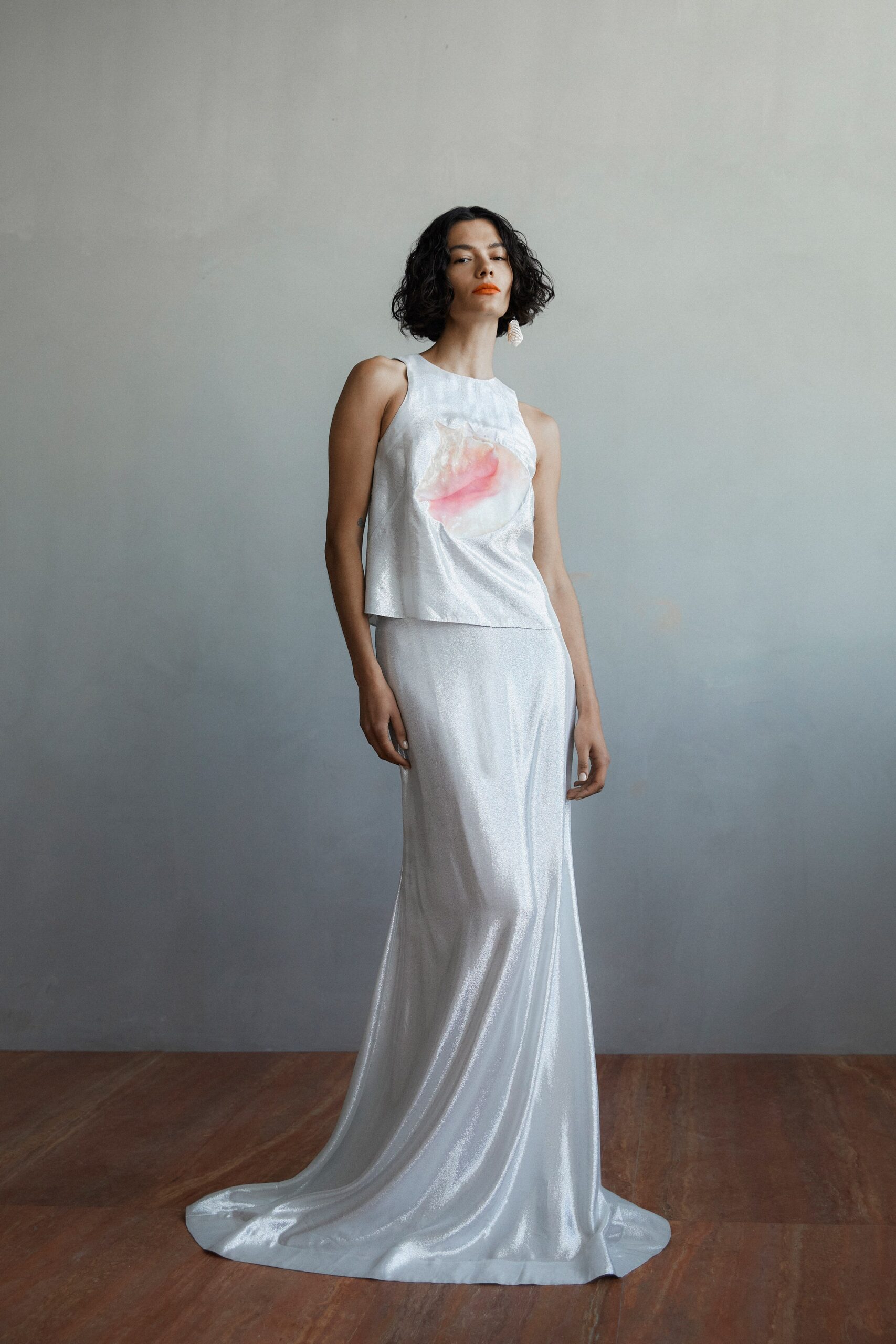A fitted silver satin sleeveless dress with a high neckline and a slit detail.
