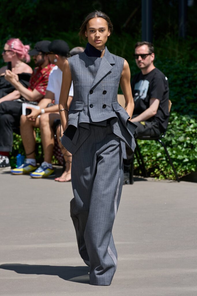 A fitted gray sleeveless blazer with an asymmetric design paired with wide-leg pants.