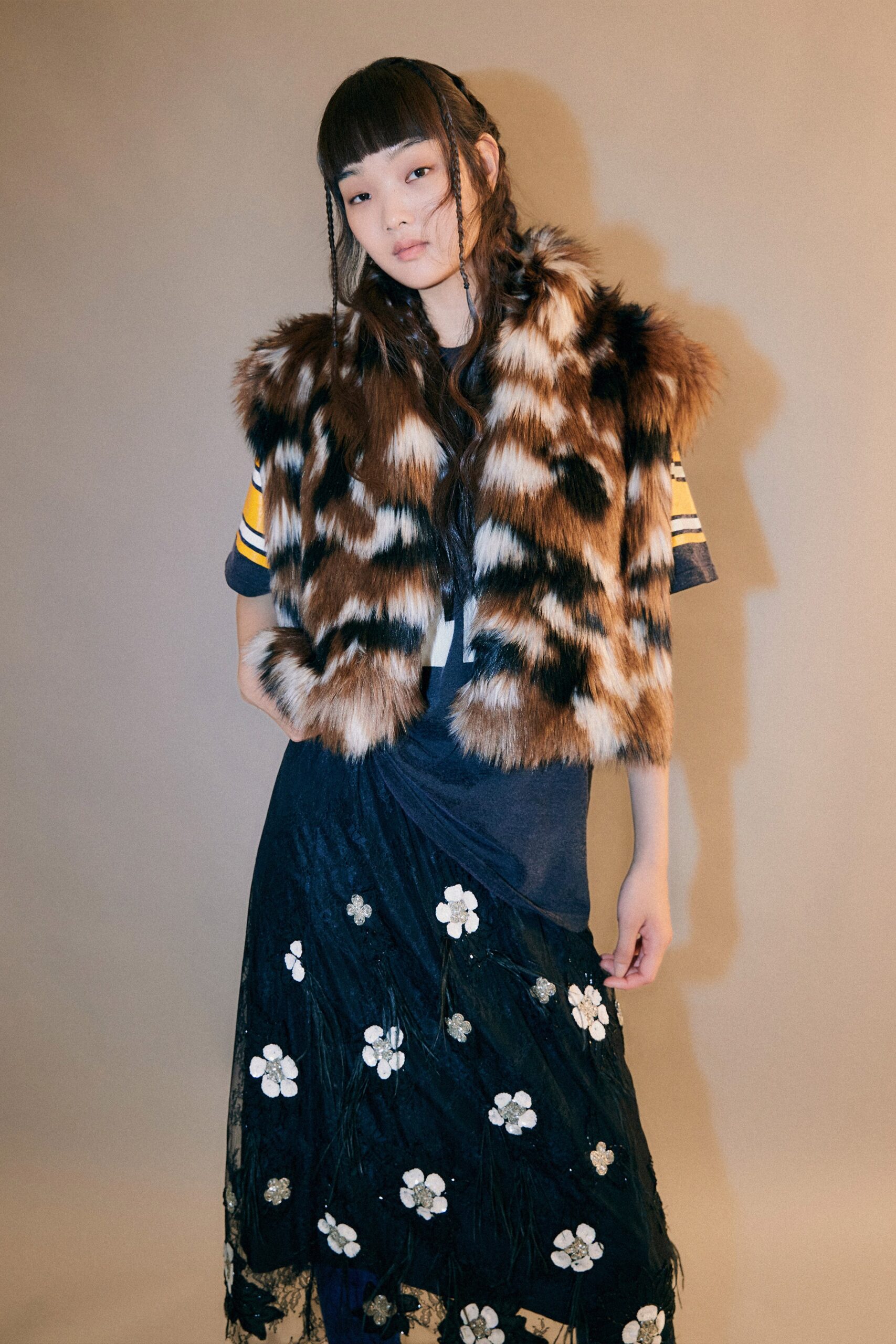 A fitted black dress layered with a sleeveless brown fur vest featuring floral details.
