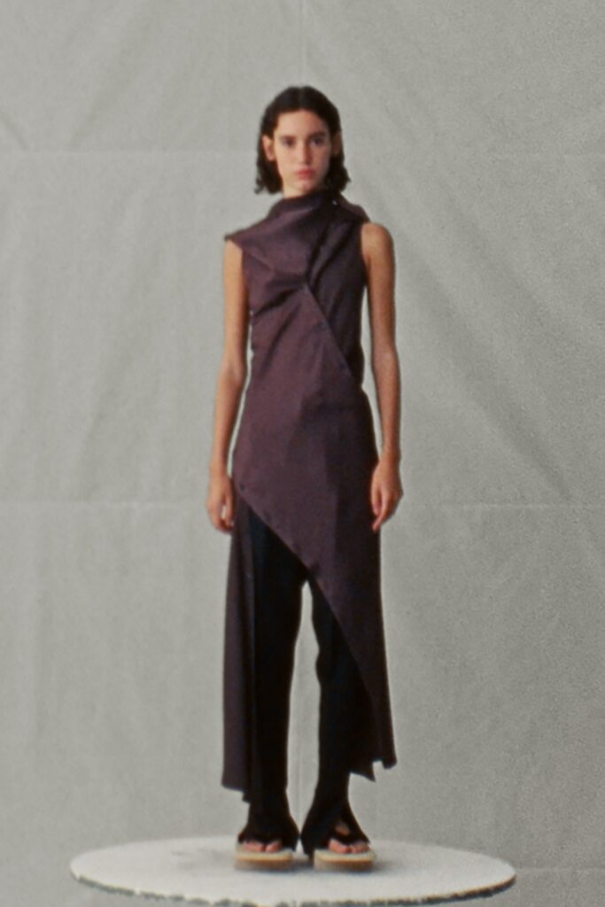 A fitted black sleeveless dress with an asymmetric design and layered detailing.