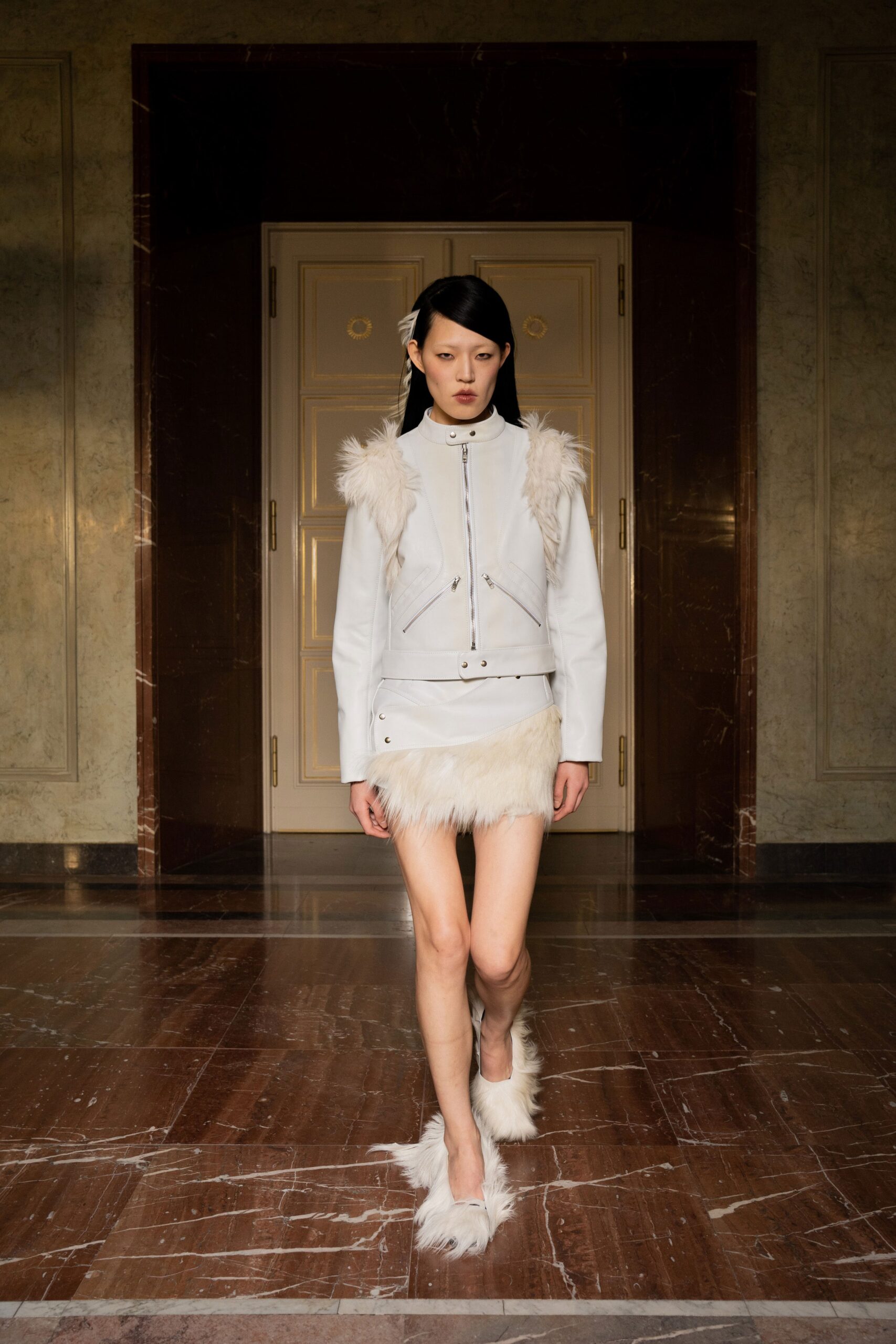 A fitted white leather jacket with a zippered front and a fringed skirt.