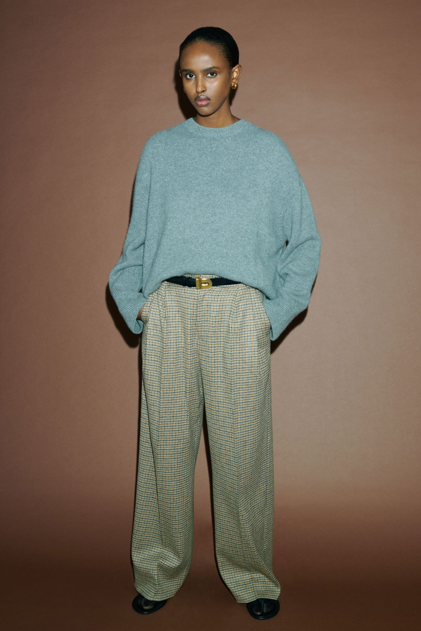 An oversized gray wool sweater paired with high-waisted beige pleated pants featuring a wide-leg silhouette.