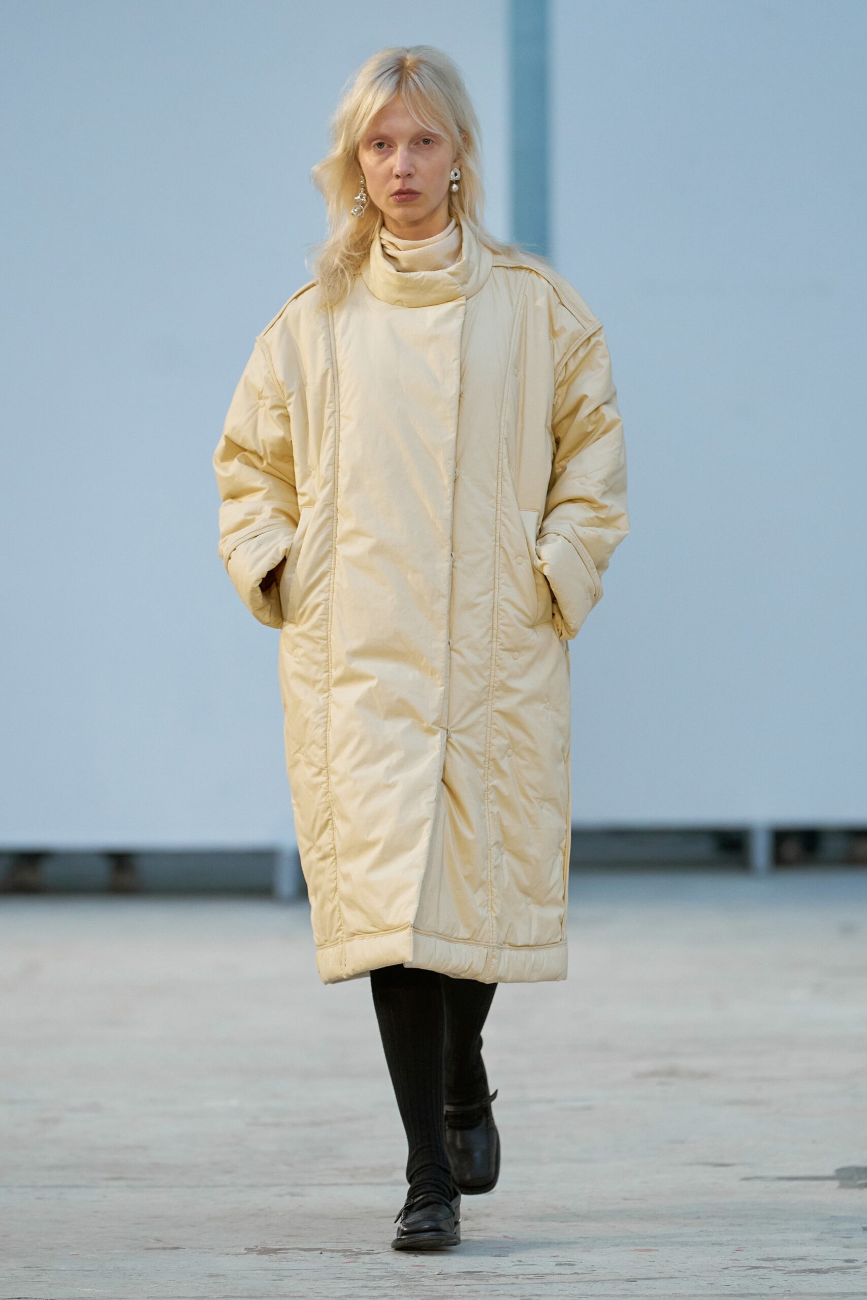An oversized beige coat with a high neckline and zippered detail, perfect for layering.