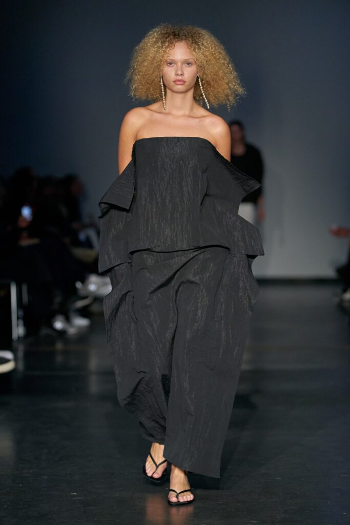 A relaxed black cotton dress with an off-shoulder design and layered details.