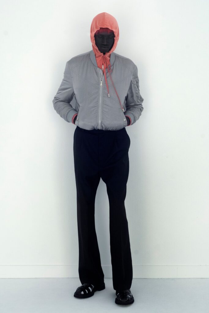 A fitted gray hooded jacket with zippered detail paired with straight-leg black pants.