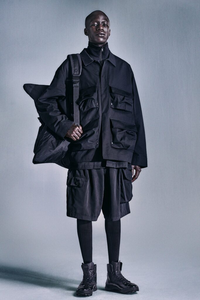 An oversized black jacket with long sleeves and pocketed design paired with black shorts.