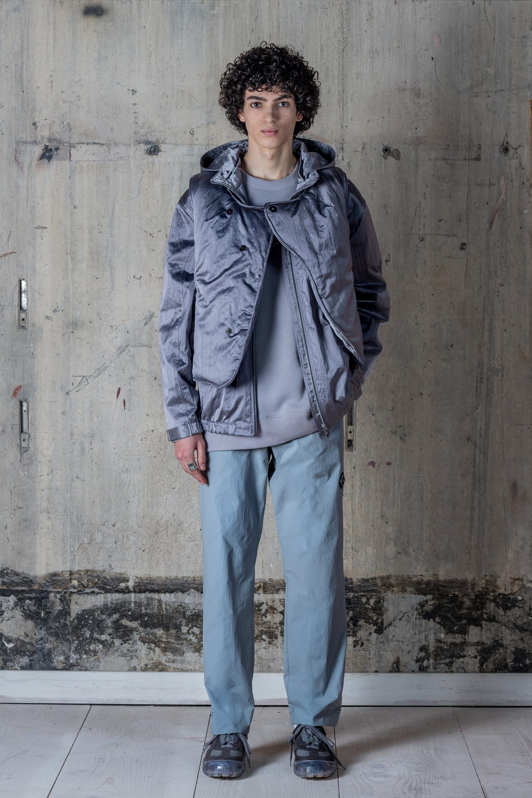 A relaxed-fit gray hooded jacket paired with blue pants featuring a zippered detail.