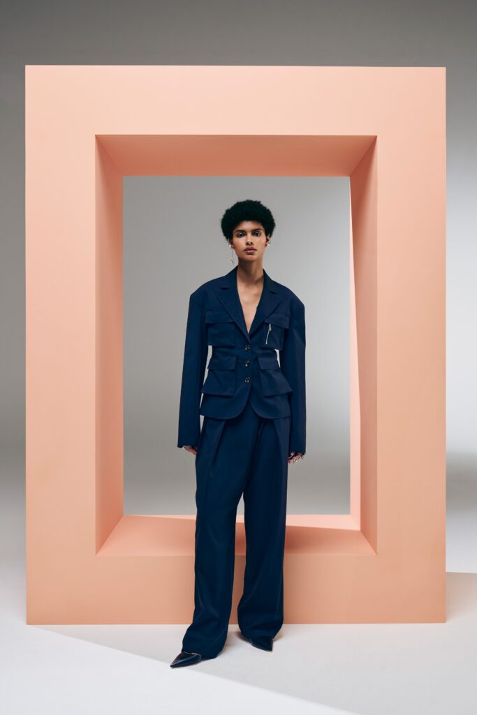 A tailored blue blazer with long sleeves and a V-neck, paired with matching pants featuring an asymmetric design.