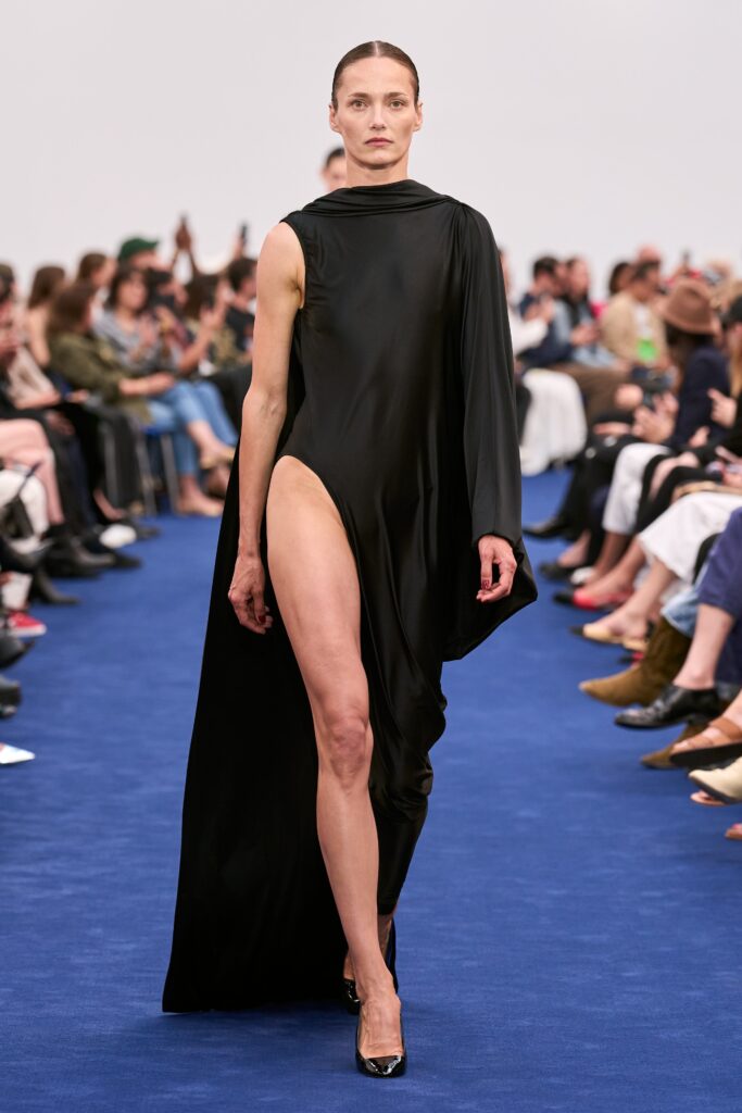 A fitted black silk dress with a high neckline and an asymmetric silhouette featuring a thigh-high slit.