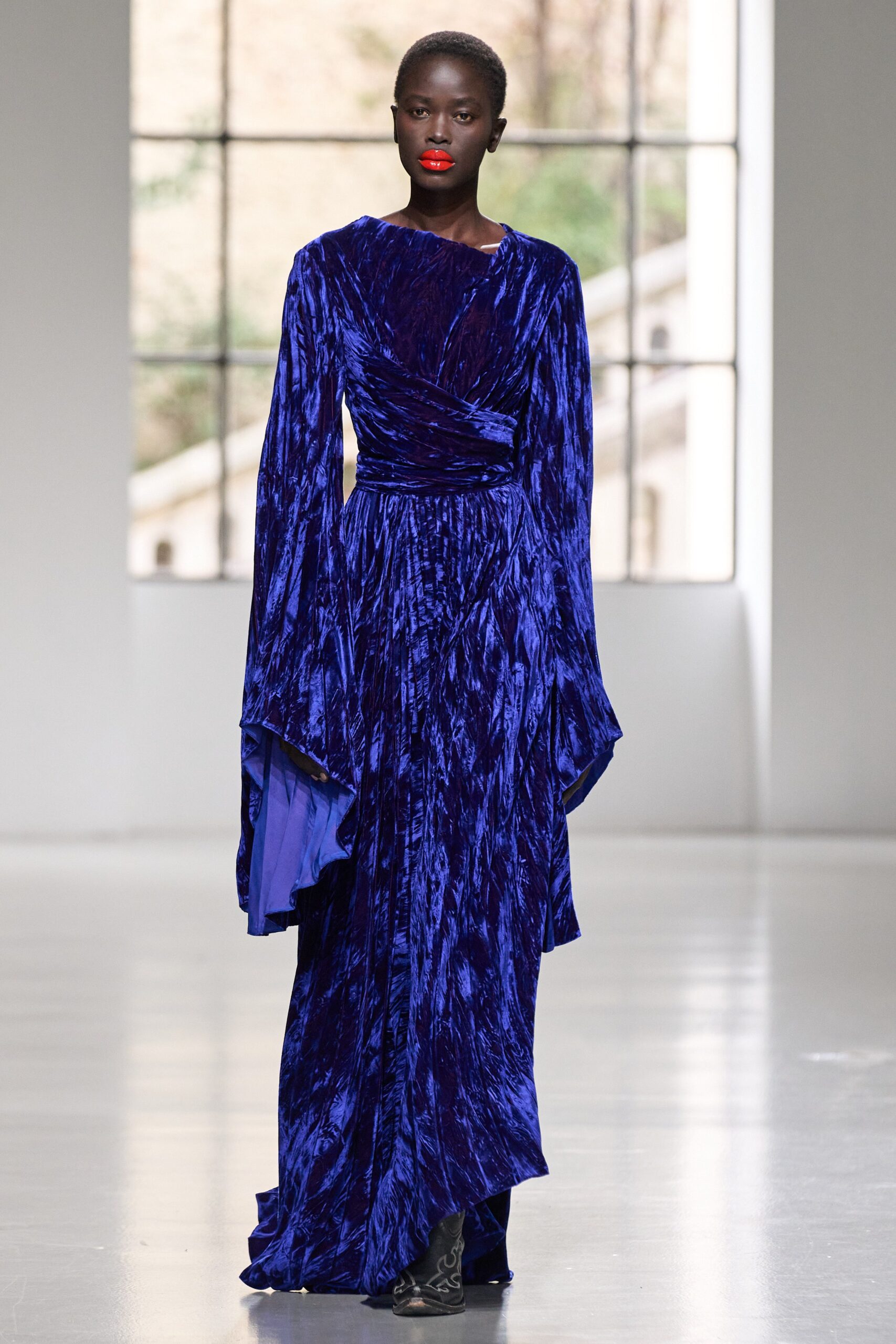 A fitted blue velvet gown with long sleeves and a V-neckline featuring a draped design.