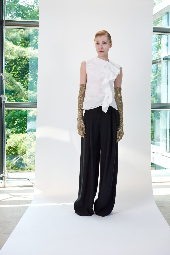 A relaxed white sleeveless top with an asymmetric design paired with black pants.