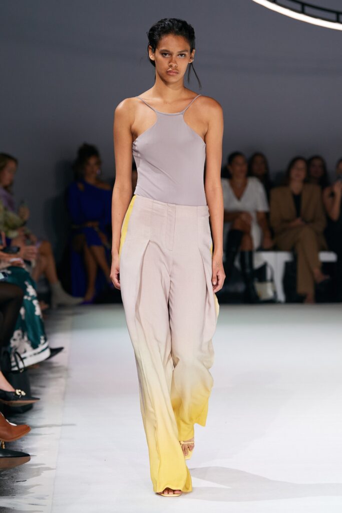 A fitted beige sleeveless top paired with pleated asymmetric pants in yellow tones.
