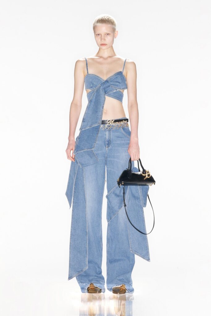 A fitted blue denim sleeveless top with asymmetric design and high-waisted layered pants.
