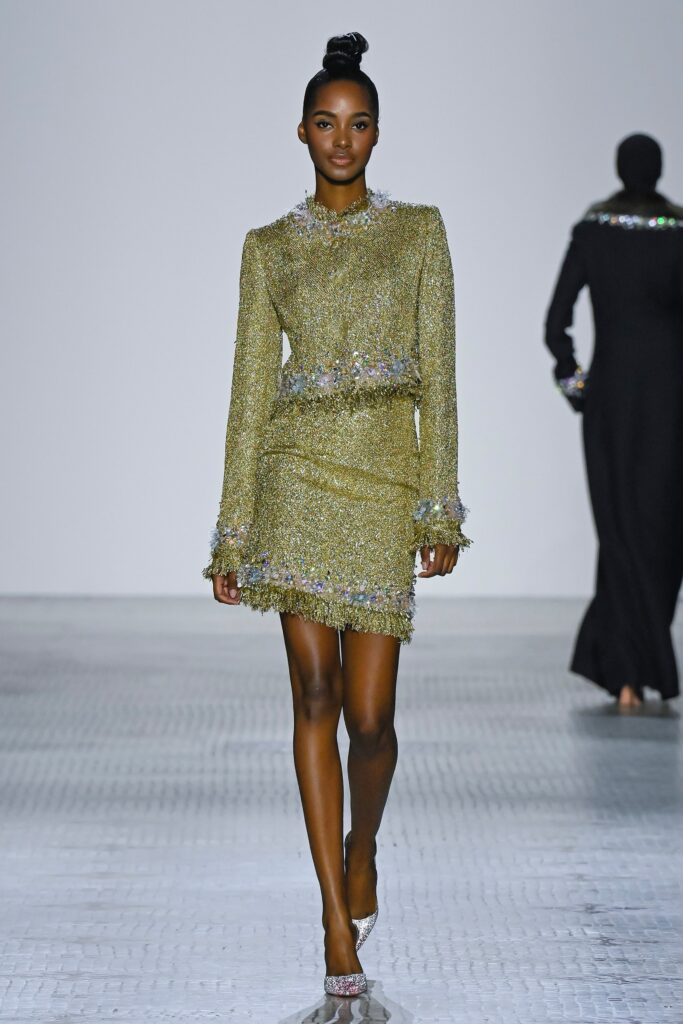 A fitted green silk dress with long sleeves, a collared neckline, and fringed embellishments.