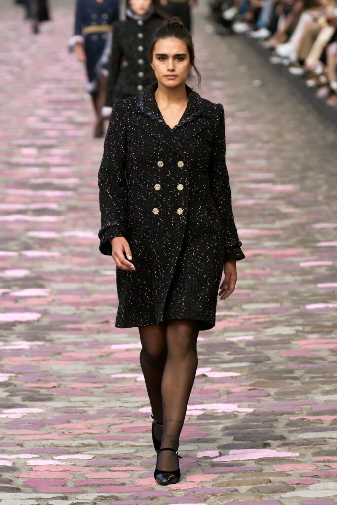 A fitted black cotton dress with long sleeves, a collared neckline, and buttoned details.