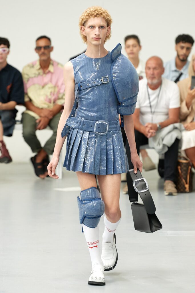 A fitted blue denim dress with a sleeveless design and pleated details.