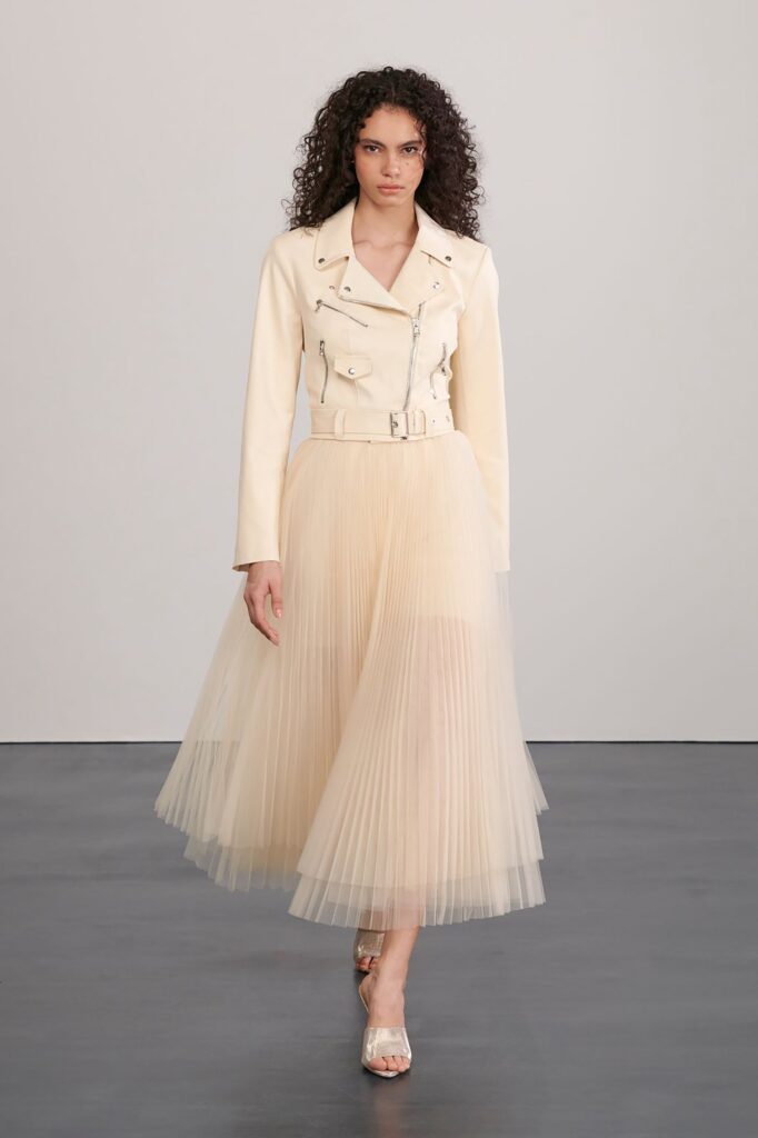 A fitted cream leather jacket paired with a pleated dress featuring a belted waist.