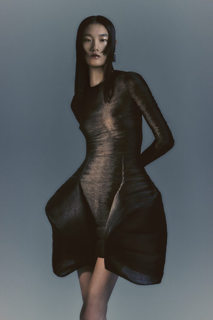 A fitted black silk dress with long sleeves and an asymmetric silhouette.