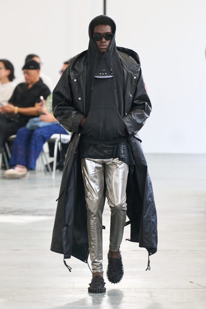 A fitted black leather coat with a hood and long sleeves paired with silver fitted pants.