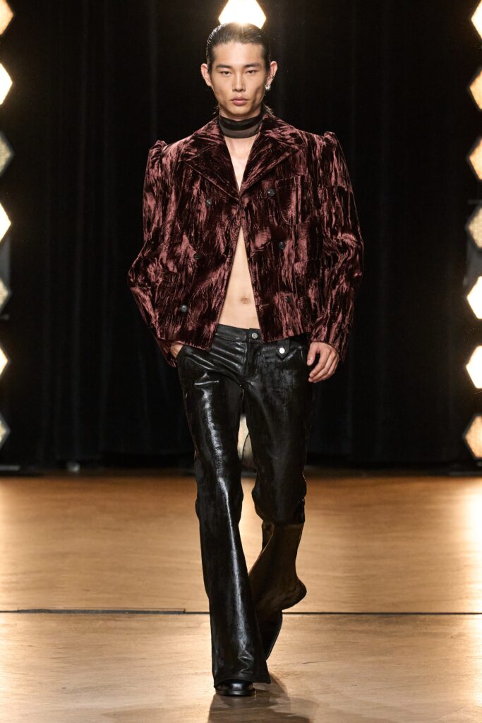 A fitted burgundy velvet jacket with long sleeves and a structured silhouette paired with black leather pants.