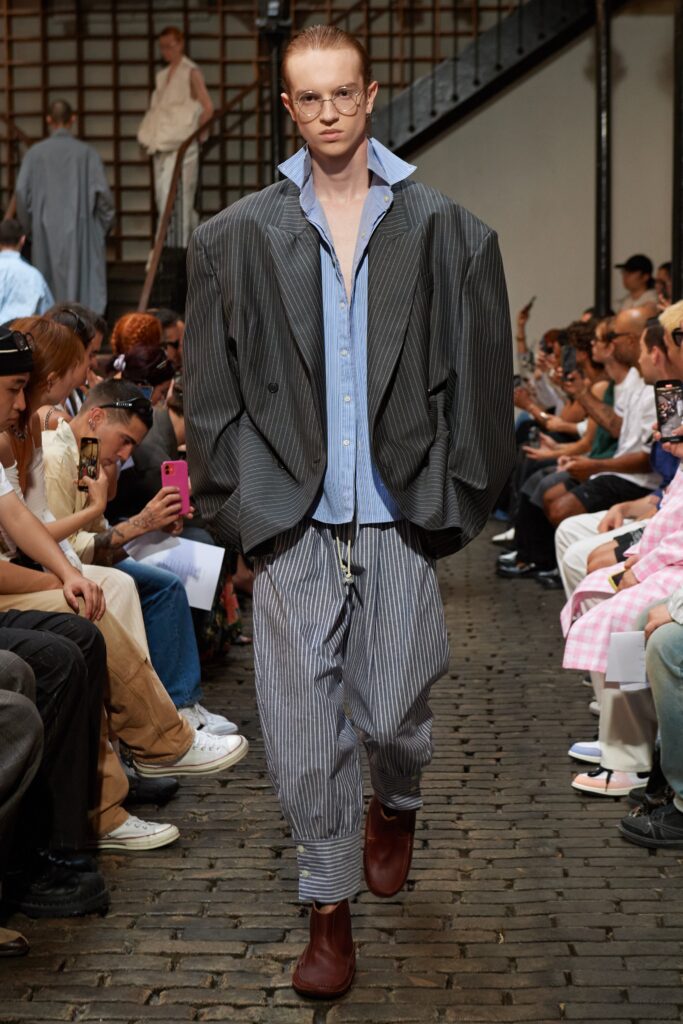 An oversized gray striped jacket paired with blue pants for a contemporary runway look.