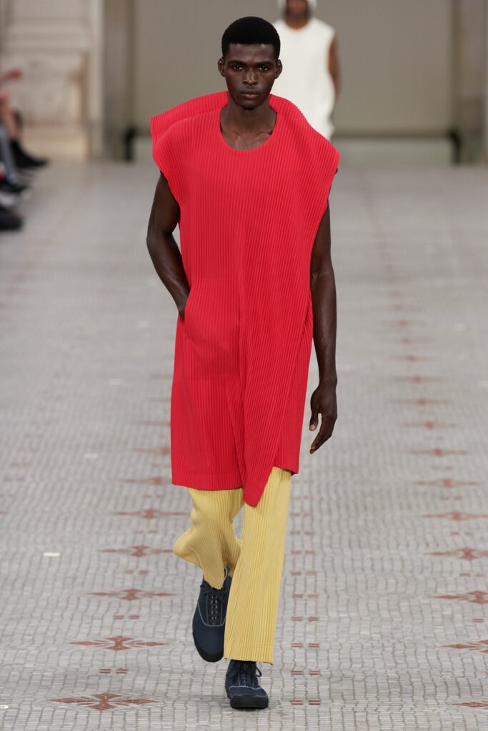 A relaxed red pleated sleeveless dress paired with yellow pants for a bold runway look.