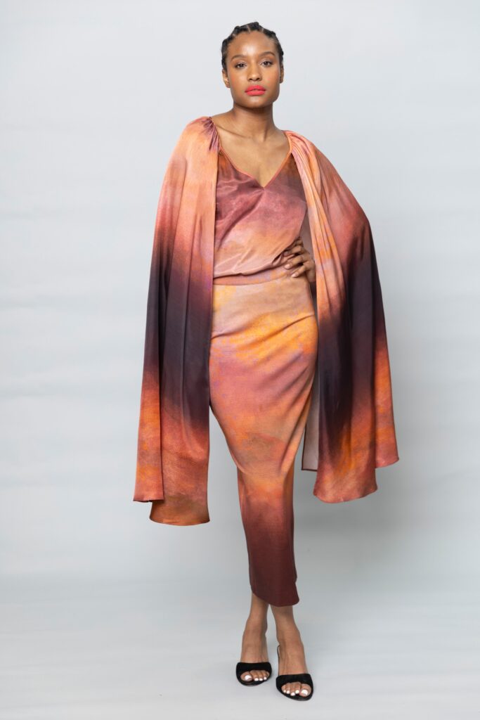 A fitted orange silk dress with a V-neckline, complemented by a layered cape.