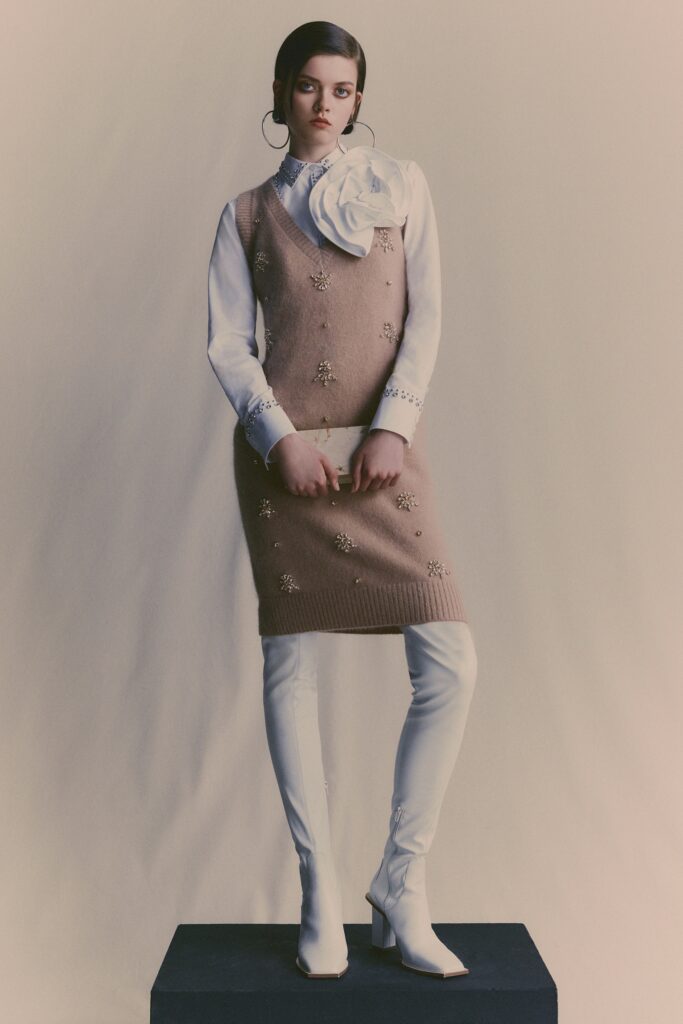 A fitted beige embroidered dress layered over a white long-sleeve shirt with a V-neckline.