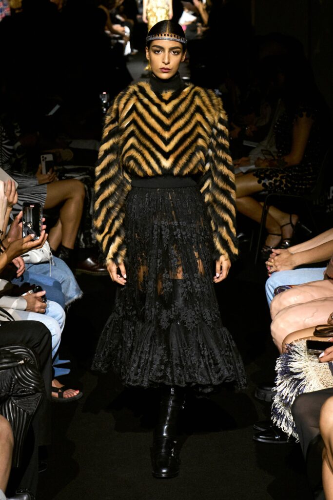 A fitted black lace dress featuring a high-neck and long sleeves, layered with fur accents.