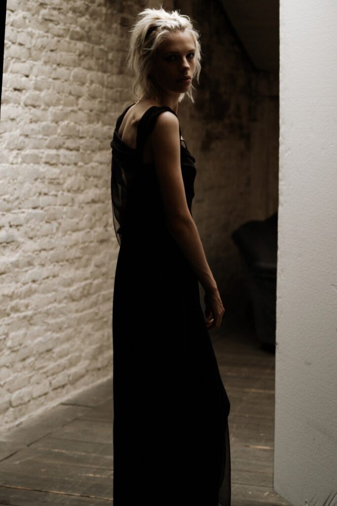 A fitted black silk sleeveless dress with a V-neckline and asymmetric design.