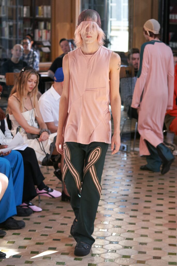 A relaxed pink cotton sleeveless top paired with green pants featuring an asymmetric design.