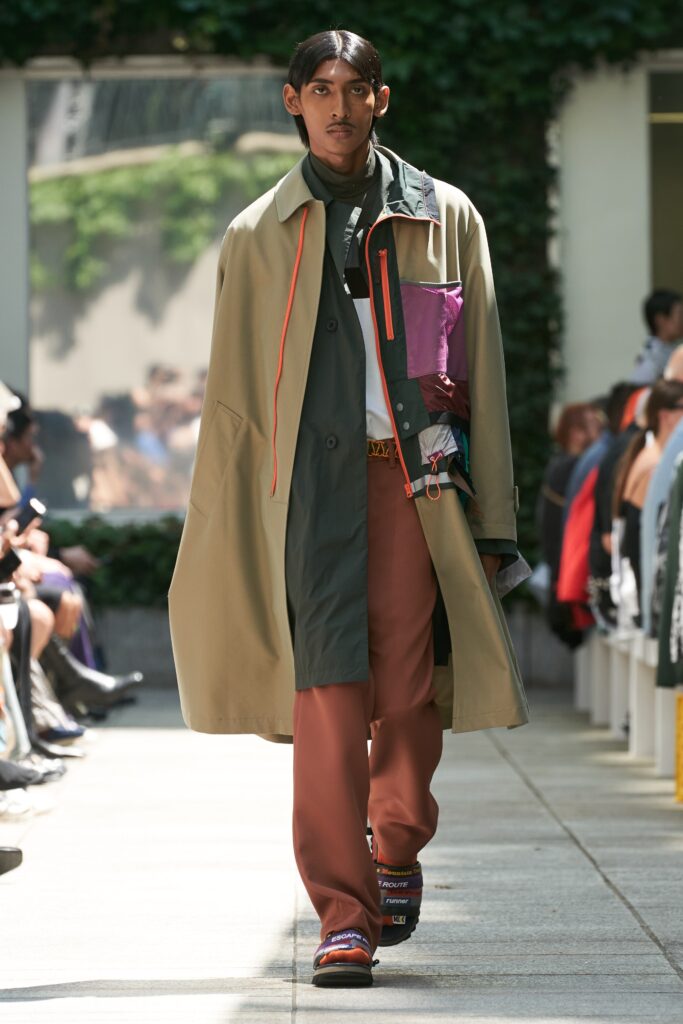 A relaxed-fit beige and green coat paired with orange pants, featuring a layered design.
