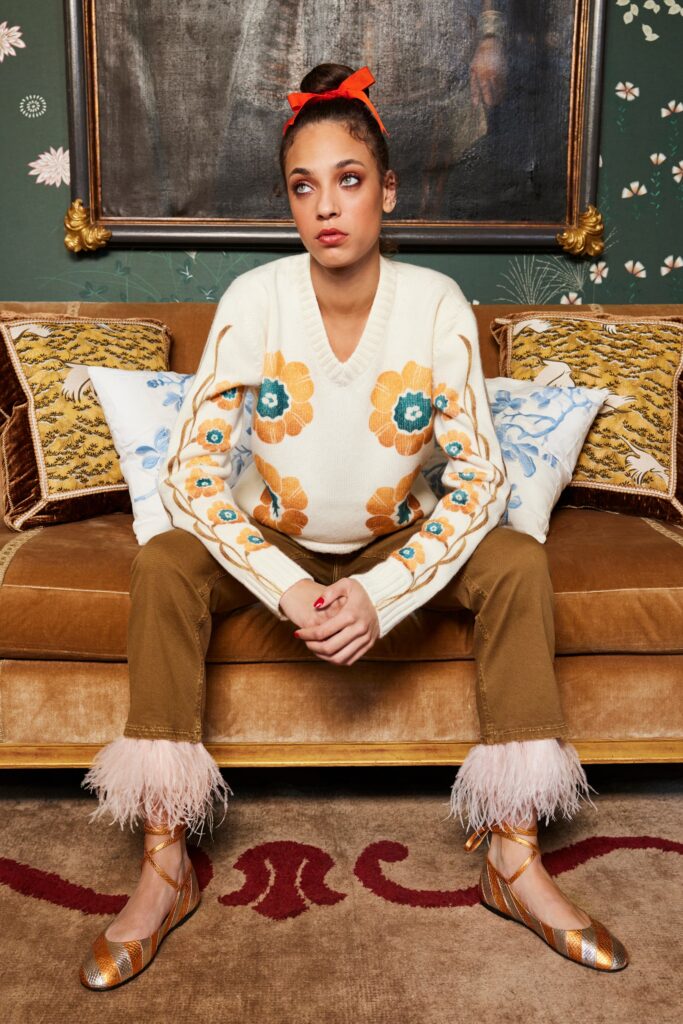 A relaxed white embroidered sweater with a V-neck paired with flared brown pants.