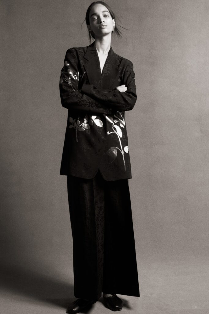 A relaxed black silk blazer with embroidery paired with wide-leg pants.