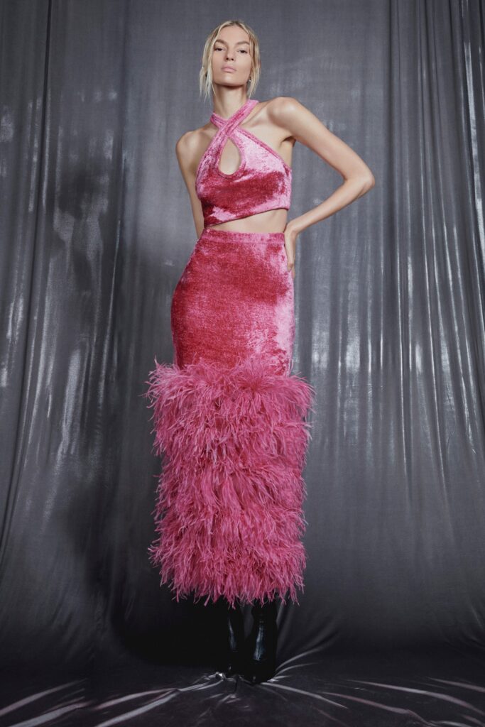 A fitted pink velvet dress with a high neckline and fringed detailing at the hem.