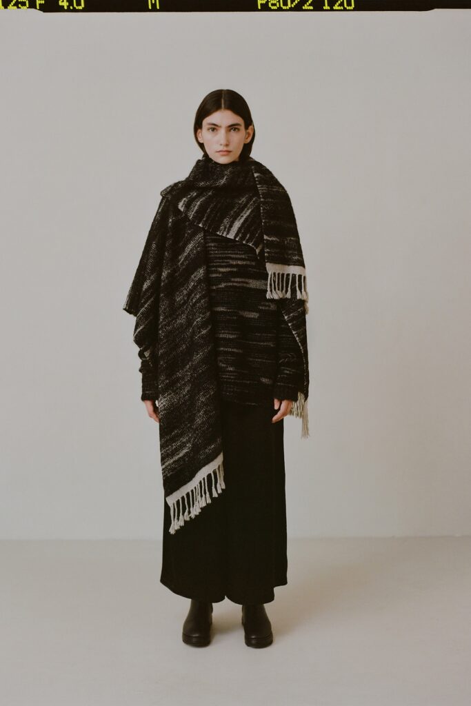 A relaxed black wool dress with a high-neck and long sleeves, featuring a layered cape design.