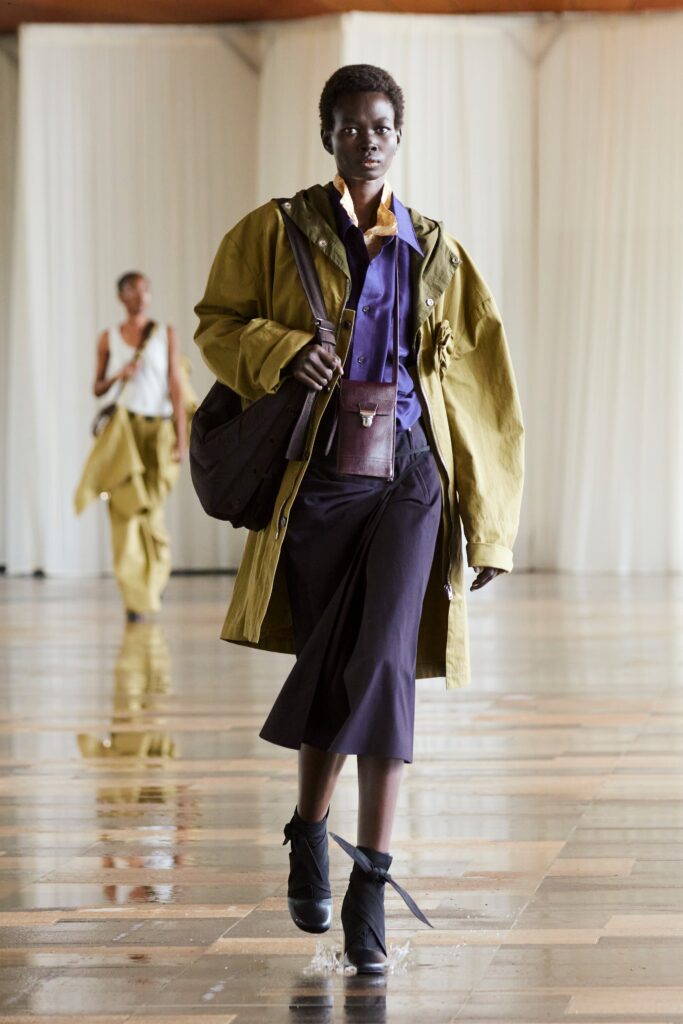 A relaxed green coat layered over a purple dress with long sleeves and an asymmetric design.