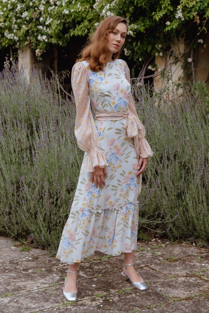 A fitted white silk dress with long sleeves, high neckline, and tiered floral design.