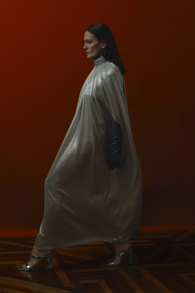 A relaxed silver silk cape with long sleeves and a high neckline, featuring a draped design.
