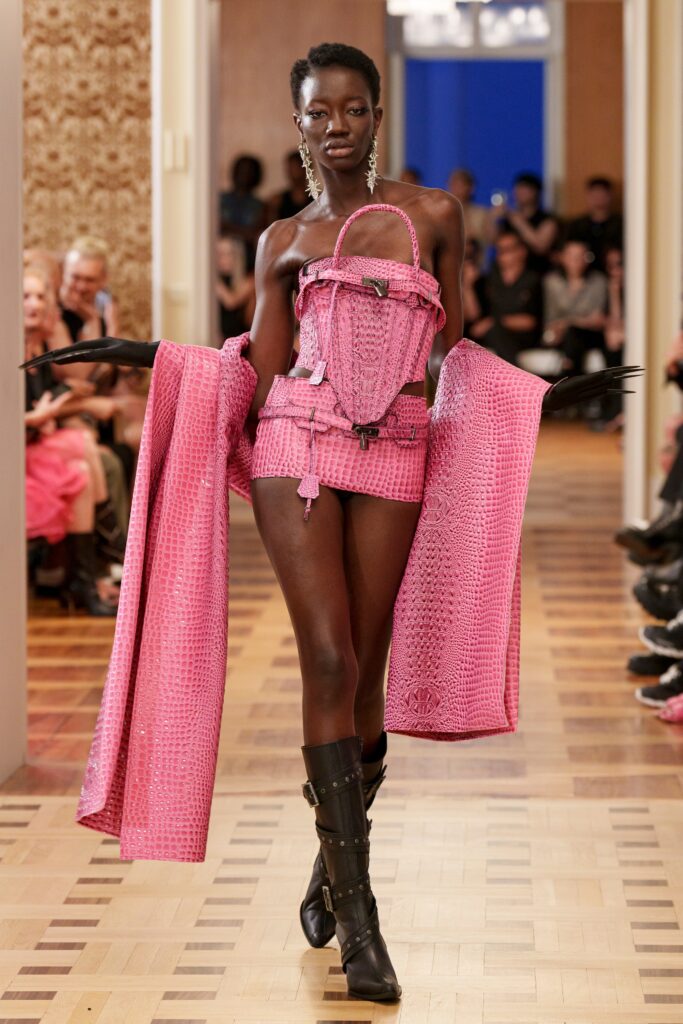 A fitted pink leather sleeveless dress paired with a matching coat, showcasing a bold fashion statement.