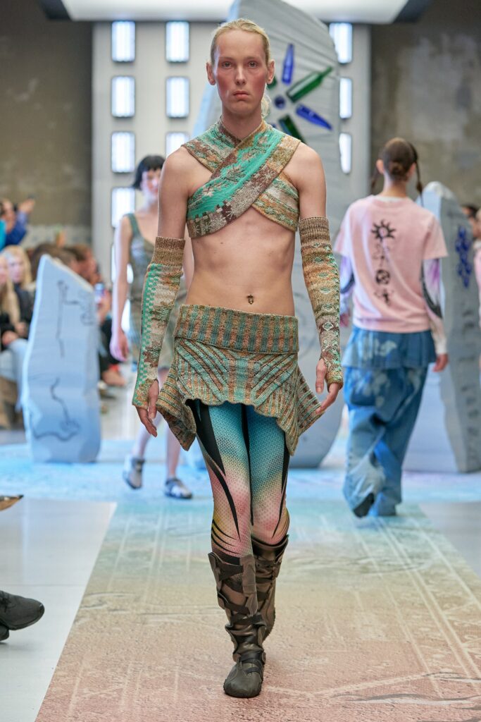 A fitted multicolor knit top with a high-neck and asymmetric layered design paired with fitted pants.