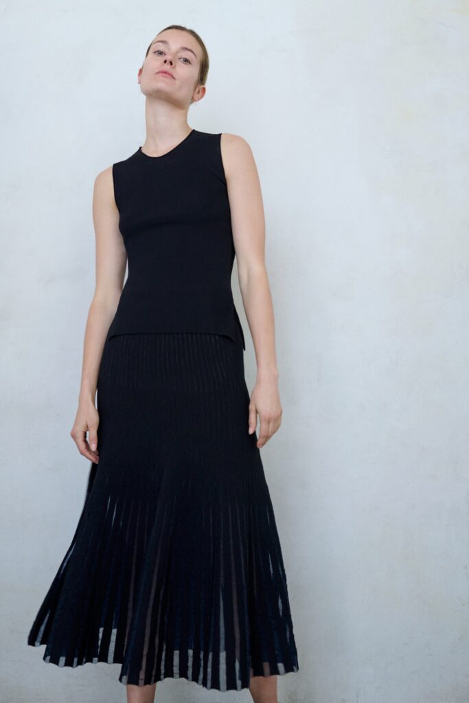 A fitted black sleeveless dress with a high-neck and pleated design.