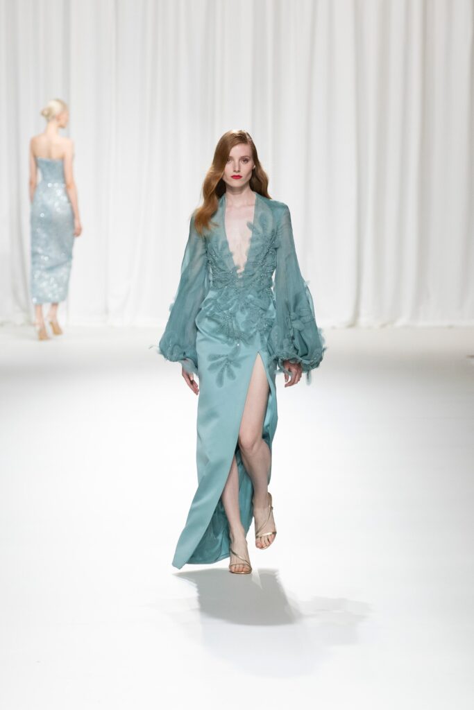 A fitted blue silk dress with long sleeves, a V-neckline, and a thigh-high slit.