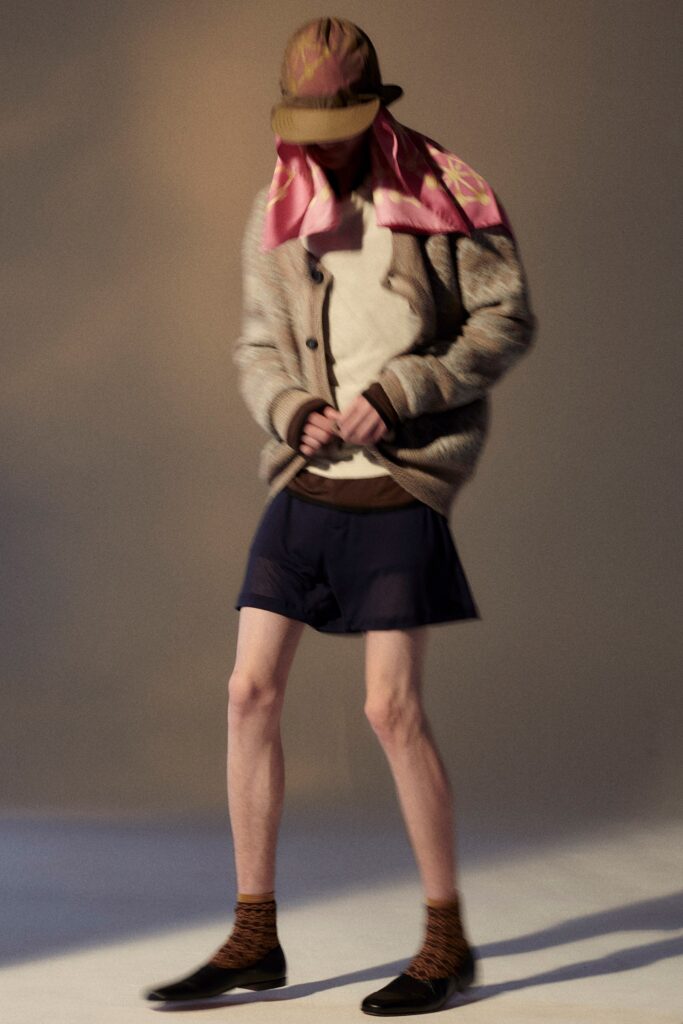 A relaxed beige wool cardigan with long sleeves paired with navy cotton shorts.