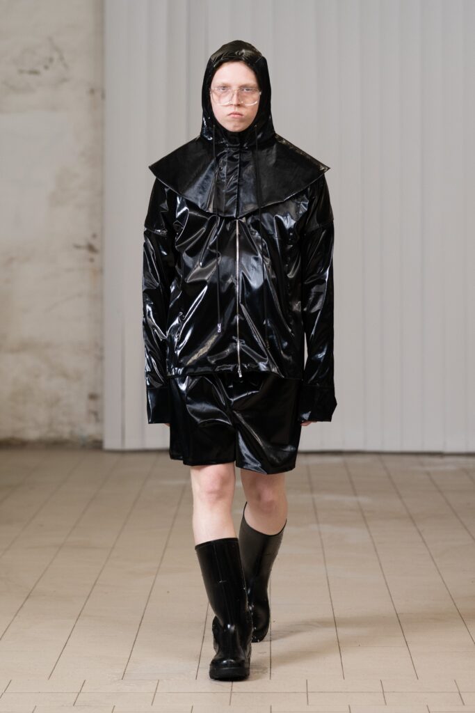An oversized black leather hooded jacket paired with matching shorts and knee-high boots.
