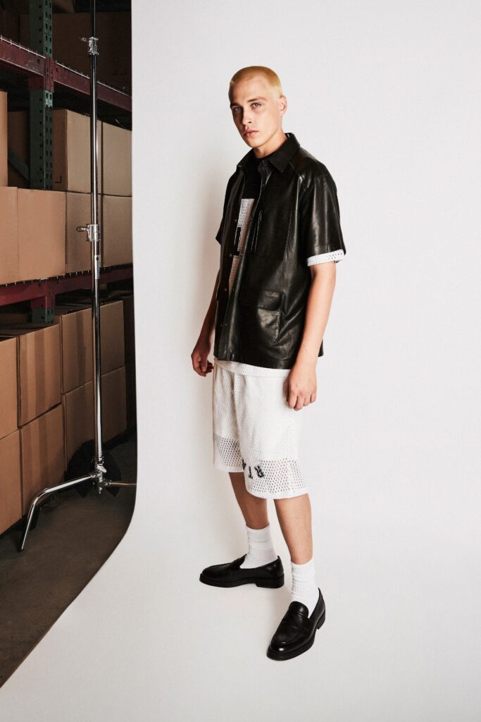 A relaxed black leather short-sleeve shirt paired with high-waisted white mesh shorts.